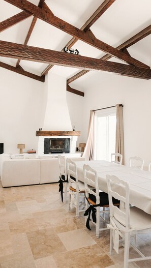 A spacious room with a high ceiling, exposed wooden beams, a fireplace, a dining table with chairs, and a window with curtains. - Maison Olivette: Provençal villa with a private pool, 6 bedrooms, and olive trees (Flayosc)