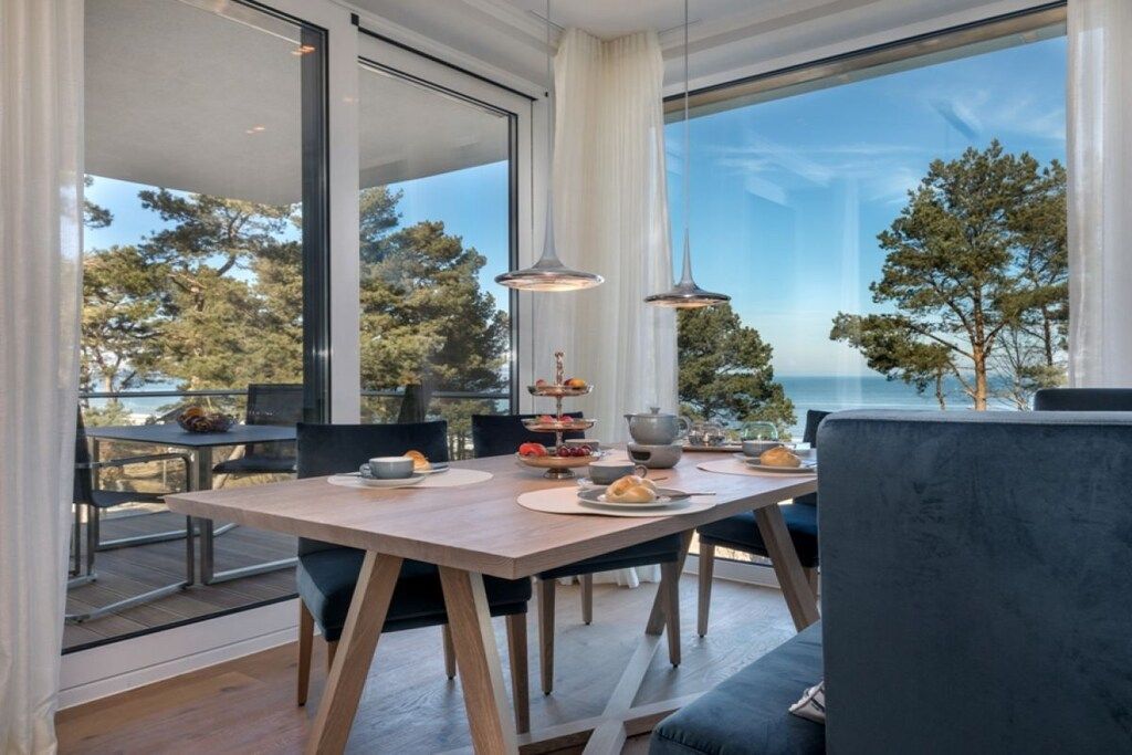A dining area with a table set for four, large windows, and a view of trees and the sea.