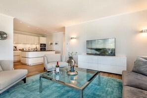 A modern living room with a glass coffee table, a sofa, a TV, and a kitchen in the background. - at Villa Vogue, Baltic Sea Dream (Binz)