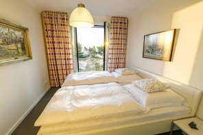 Ein Schlafzimmer mit einem Bett, zwei Kissen, einem Nachttisch, einer Lampe und einem Fenster mit Vorhängen.