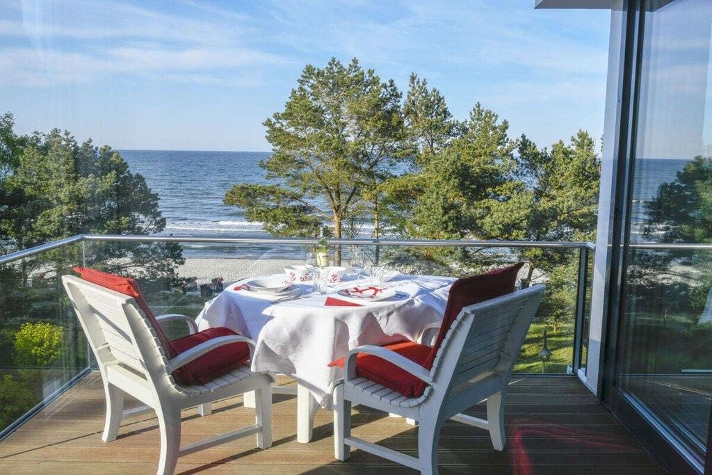 A balcony with a table set for dining, overlooking a beach and ocean.