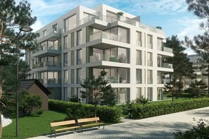 Ein modernes, mehrgeschossiges Gebäude mit Balkonen, umgeben von Grünflächen und einem gepflasterten Weg.