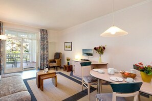 A well-lit living room with a sofa, a dining table set for two, a television, and a window with curtains. - "Bella Vista" at Villa Seeadler (Binz)