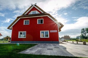 Ein rotes Haus mit einem Satteldach, einer gepflasterten Auffahrt und einem Rasen.