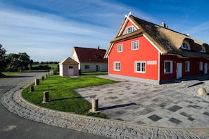 Une maison rouge avec un toit de chaume, une allée pavée et une pelouse bien entretenue.