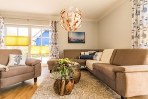 Ein Wohnzimmer mit einer braunen Sofagarnitur, einem Glastisch mit Holzfuß und einer hängenden, kugelförmigen Leuchte.