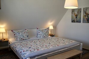A bedroom with a bed, two bedside lamps, a bench, and floral artwork on the wall. - Thatched House "Seagull Emma" (Zierow)