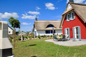 Ein Haus mit einem Strohdach, rotem Anstrich und einer Terrasse mit Gartenmöbeln.