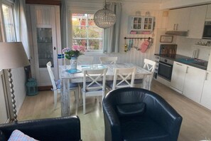A dining area with a table set for four, white chairs, a black leather chair, a hanging light fixture, and a window with curtains. - Holiday home with 3 bedrooms (Boltenhagen)