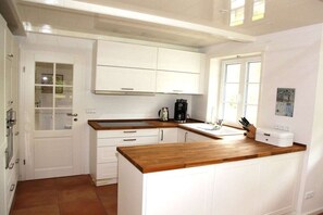 A kitchen with white cabinets, a wooden countertop, and a coffee maker. - "Friesenhaus Hensen" (Nebel)