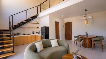 Un espacio habitable moderno con una escalera, un sofá, una mesa de comedor y una zona de cocina.