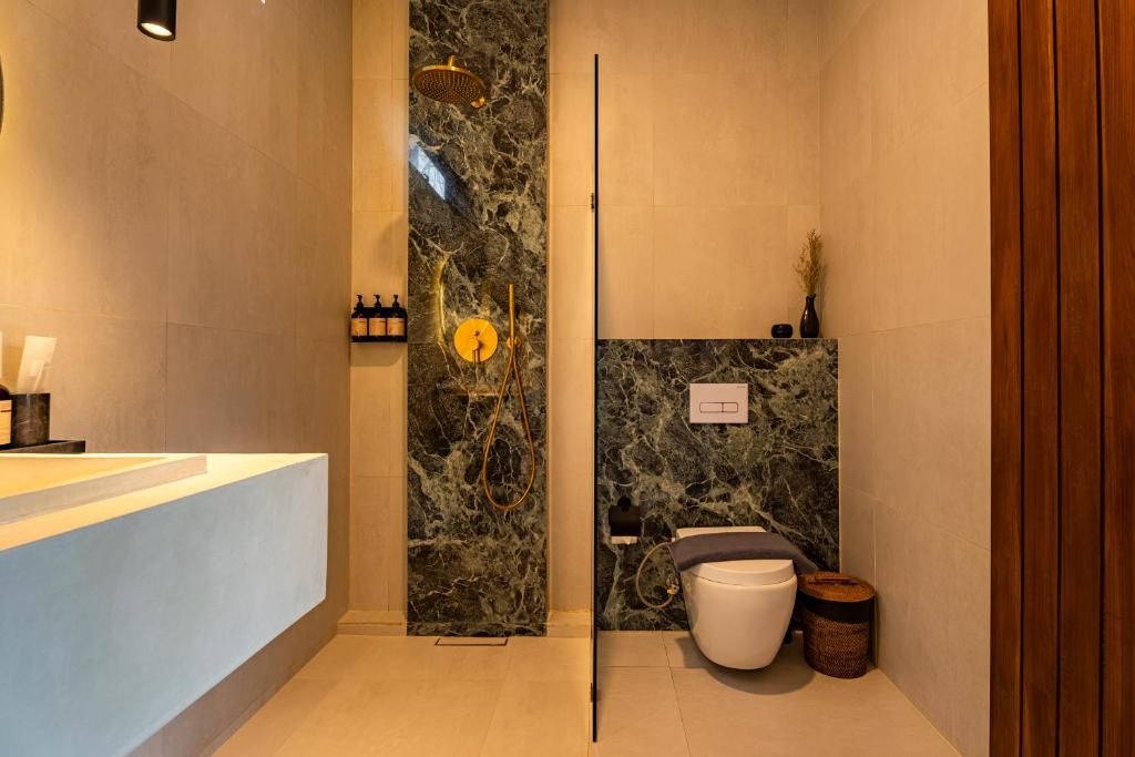 A modern bathroom with a marble wall, a shower, a toilet, and a sink with toiletries.