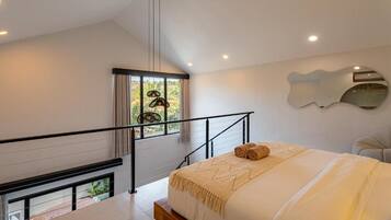 A modern bedroom with a large bed, a view of greenery through a window, a staircase, and a unique wall mirror.