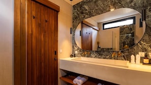 Un baño moderno con puerta de madera, salpicadero de mármol, un espejo grande y un lavamanos empotrado.