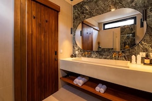 A modern bathroom with a wooden door, a marble sink, and a large mirror. - Eala Estate (Pujut, Central Lombok Regency)
