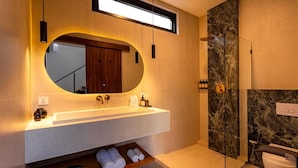 A modern bathroom with a large mirror, a built-in sink, a shower, and a shelf with towels. - Eala Estate (Pujut, Central Lombok Regency)