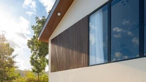 Una casa moderna con terraza de madera, piscina y un ventanal grande.