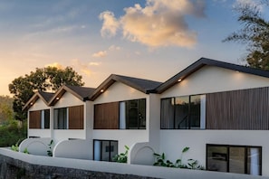 A modern multi-story building with a flat roof, large windows, and a stone retaining wall. - Eala Estate (Pujut, Central Lombok Regency)