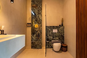 Een moderne badkamer met een marmeren wand, een douche, toilet en wastafel.