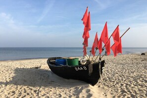A boat with red flags on a sandy beach. - Villa Poseidon 02 - East Wind (Ostseebad Binz)