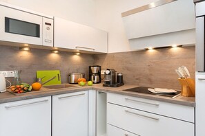 Een moderne keuken met witte kastjes, een magnetron, een koffiezetapparaat en een snijplank.