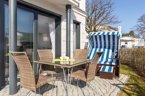 An outdoor patio with wicker furniture and a striped awning. - Villa Poseidon 02 - East Wind (Ostseebad Binz)