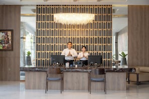 A reception desk with two staff members, a chandelier, and a patterned wall. - Lynn Hotel Jombang (Jombang)