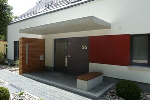 Un bâtiment moderne doté d’un toit plat, avec le chiffre « 26 » inscrit sur la façade et un petit banc à l’extérieur.
