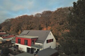 A modern two-story house with a red and white facade, a balcony, and solar panels on the roof. - 14° EAST Holiday Apartment 1 (Koserow)