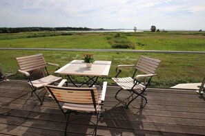 An outdoor deck with a table and chairs, overlooking a grassy field and water. - Holiday home in Usedom with 4 bedrooms (Zinnowitz)