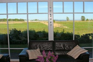 Et værelse med en sort lædersofa, der vender ud mod et stort vindue med udsigt over et grønt mark.