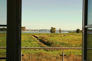 A view through a window of a grassy field with a body of water and boats in the distance. - Holiday home in Usedom with 4 bedrooms (Zinnowitz)