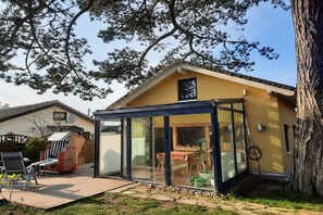 A house with a glass-enclosed patio area, a dining table, and a chair. - Holiday home in Travemünde with Wi-Fi (Travemünde)