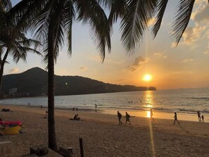 Ein Strand mit Palmen, einem Sonnenuntergang und Menschen, die am Sand entlanggehen.