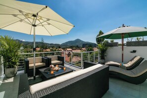 A rooftop terrace with outdoor furniture, a table with a tray of items, and a view of a mountain and buildings. - Tropical Kamala Townhouse w/Pool (KP54) (Kathu)