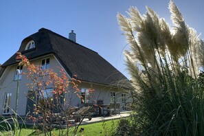 Ein Haus mit einem Strohdach, einer Veranda und einem Auto auf der Einfahrt.