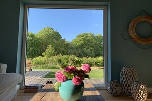 A room with a large window, a teal vase with pink flowers, and wicker lamps on the floor. - Holiday home with 1 bedroom (Groß Schwansee)