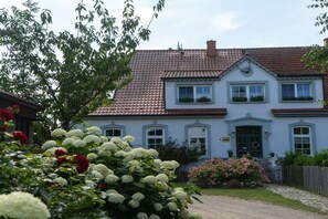 Ein zweistöckiges Gebäude mit einem Ziegeldach, einem Hauseingang mit einer Tür und einer kleinen Veranda.