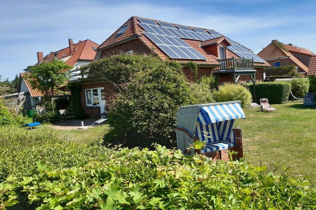 Una propiedad residencial con paneles solares en el techo, un jardín bien cuidado y un patio con una silla a rayas.