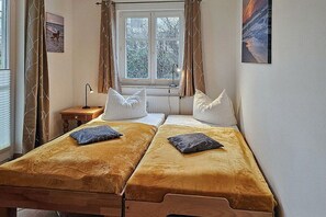 Ein Zimmer mit zwei Betten, einem fenster mit Vorhängen, einer Lampe und einer Heizung.