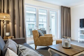 A modern living room with a sofa, armchair, and coffee table, a lamp, and a TV on a cabinet. - Sea view villa no. 15 (Großenbrode)