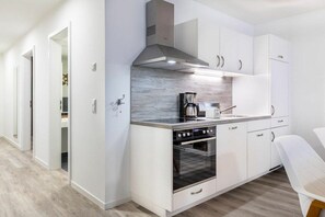 A modern kitchen with white cabinetry, a stainless steel range hood, a built-in oven, and a coffee maker. - Sea view villa no. 15 (Großenbrode)