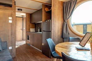 A compact kitchen with a built-in refrigerator, a dining table with chairs, and a window with curtains. - Mobile home with 2 bedrooms (Großenbrode)