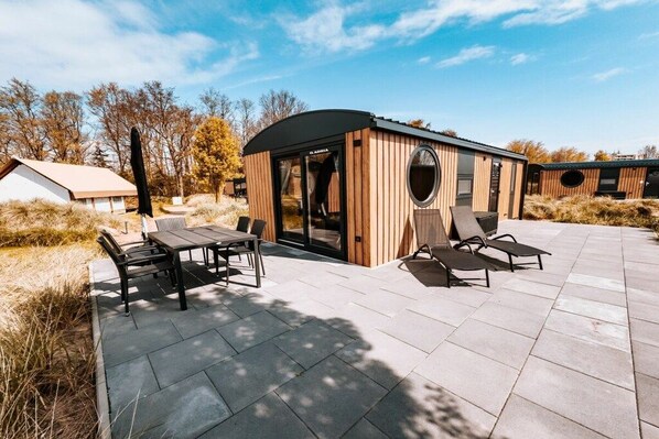 A modern outdoor patio with a wooden structure, a table with chairs, and a lounge area with sun loungers. - Mobile home with 2 bedrooms (Großenbrode)