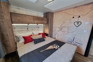 A bedroom with a wooden headboard, a bed with multiple pillows, a map on the wall, and a compass. - Mobile home with 2 bedrooms (Großenbrode)