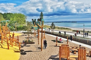 A beachside playground with play structures, a sandy area, and a walking path. - Mobile home with 2 bedrooms (Großenbrode)
