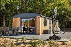 A modern outdoor seating area with a wooden structure, a table with chairs, and a statue. - Mobile home with 2 bedrooms (Großenbrode)