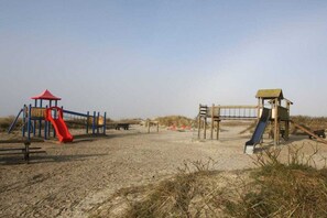 A sandy beach with a playground featuring slides and a small shelter. - Holiday home in Goting with swimming pool (Goting)