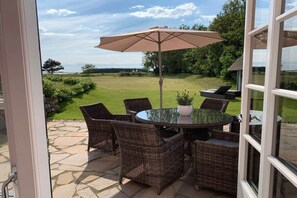 An outdoor patio with wicker furniture and a table, overlooking a grassy area. - Holiday home in Goting with swimming pool (Goting)