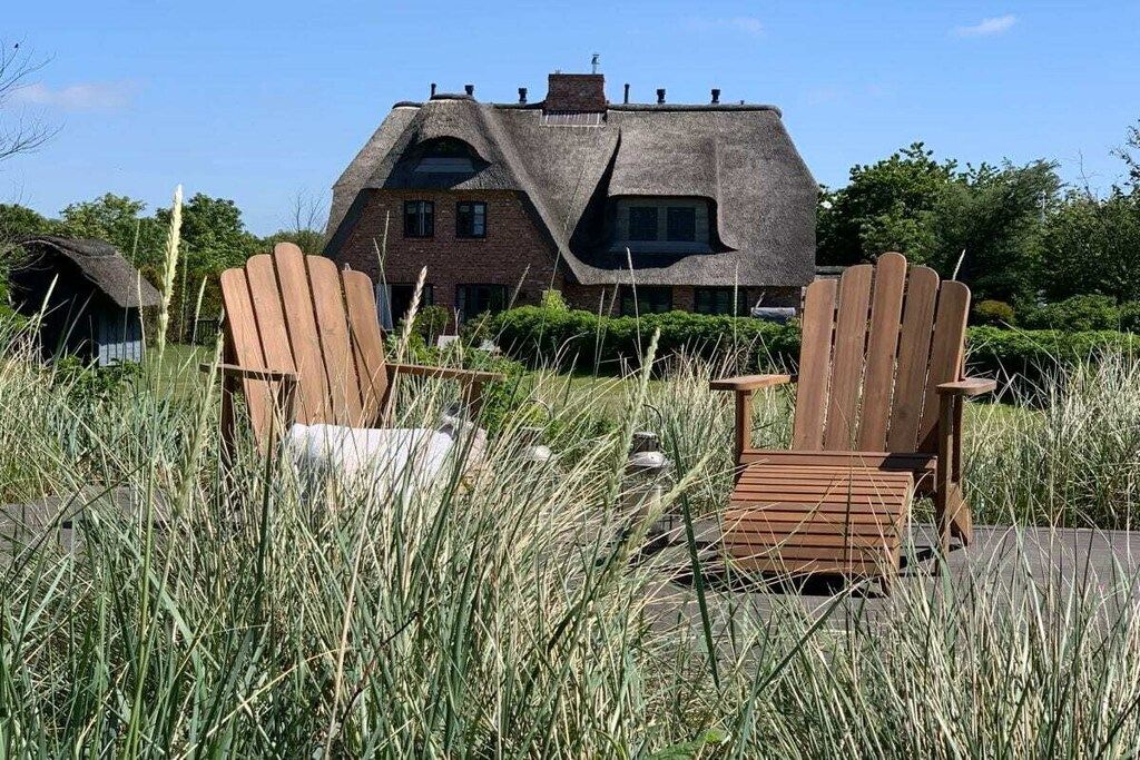 A thatched-roof house with two wooden chairs in front.